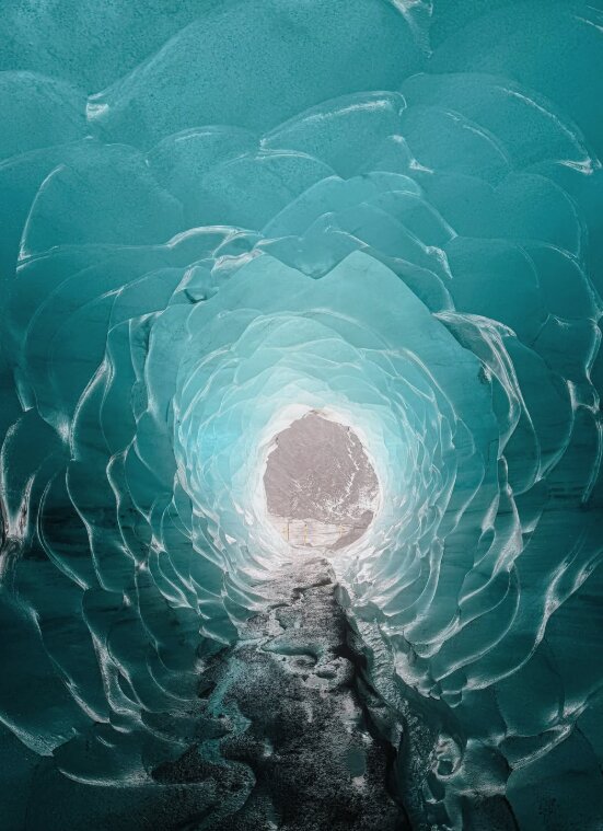 A turquoise ice tunnel narrowing toward a bright opening
