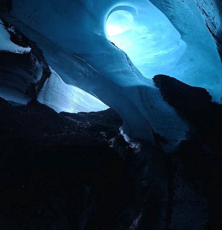 A bright blue opening in the roof of a dark ice chamber
