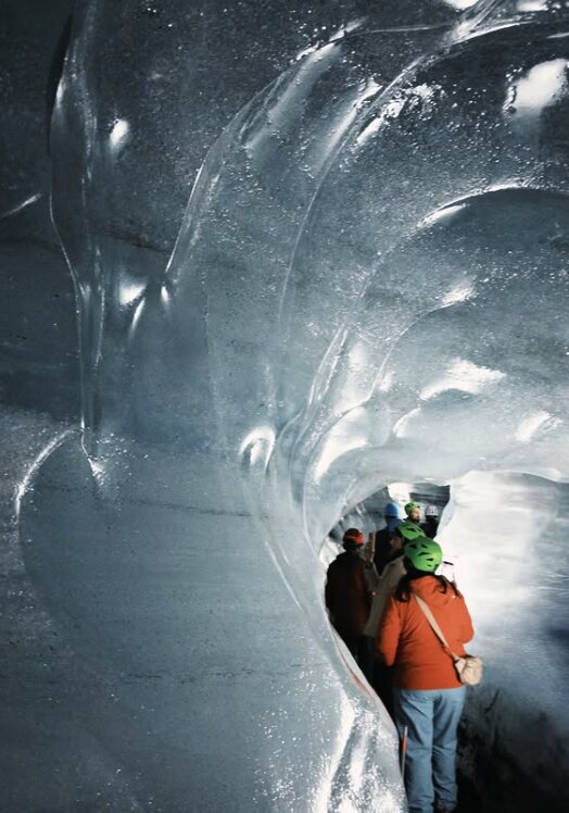 Visitors in helmets walking single file through an ice tunnel