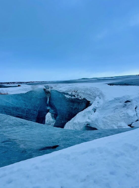 A cave opening breaking through a snow-covered glacier surface