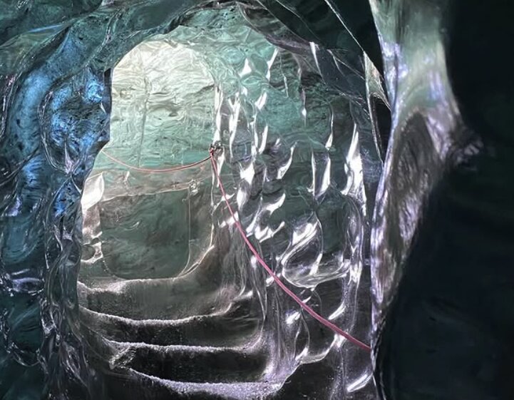 Stepped passage through clear and teal glacier ice with a guide rope