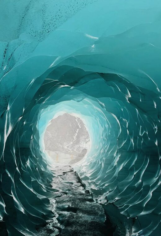 Rippled turquoise walls of an ice tunnel with a gravel floor leading out